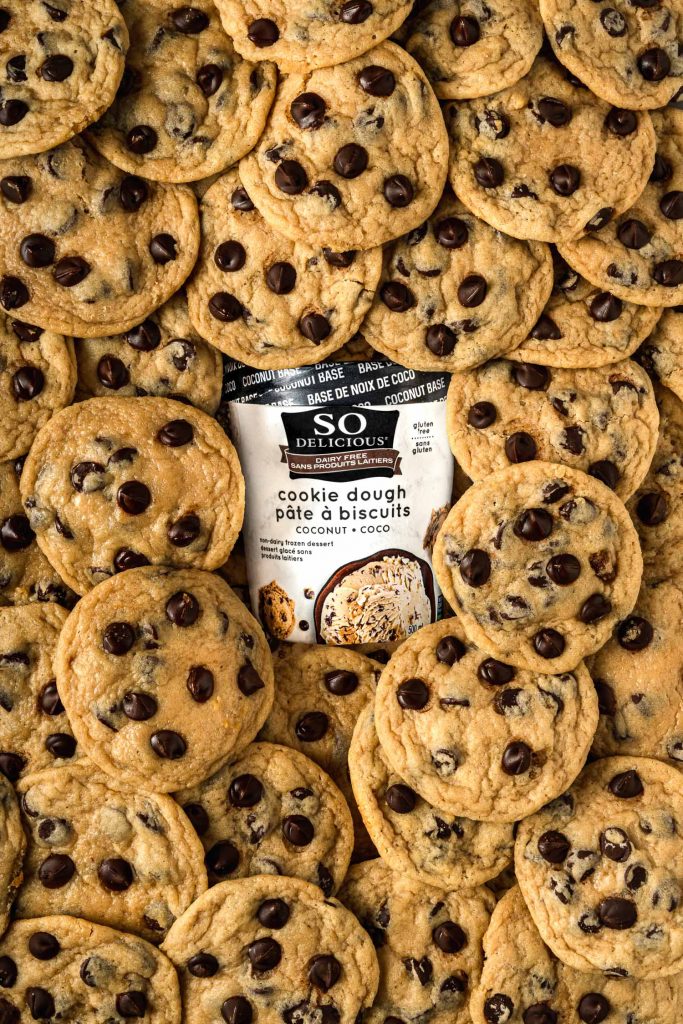 Tub of so delicious cookie dough ice cream surrounded by chocolate chip cookies