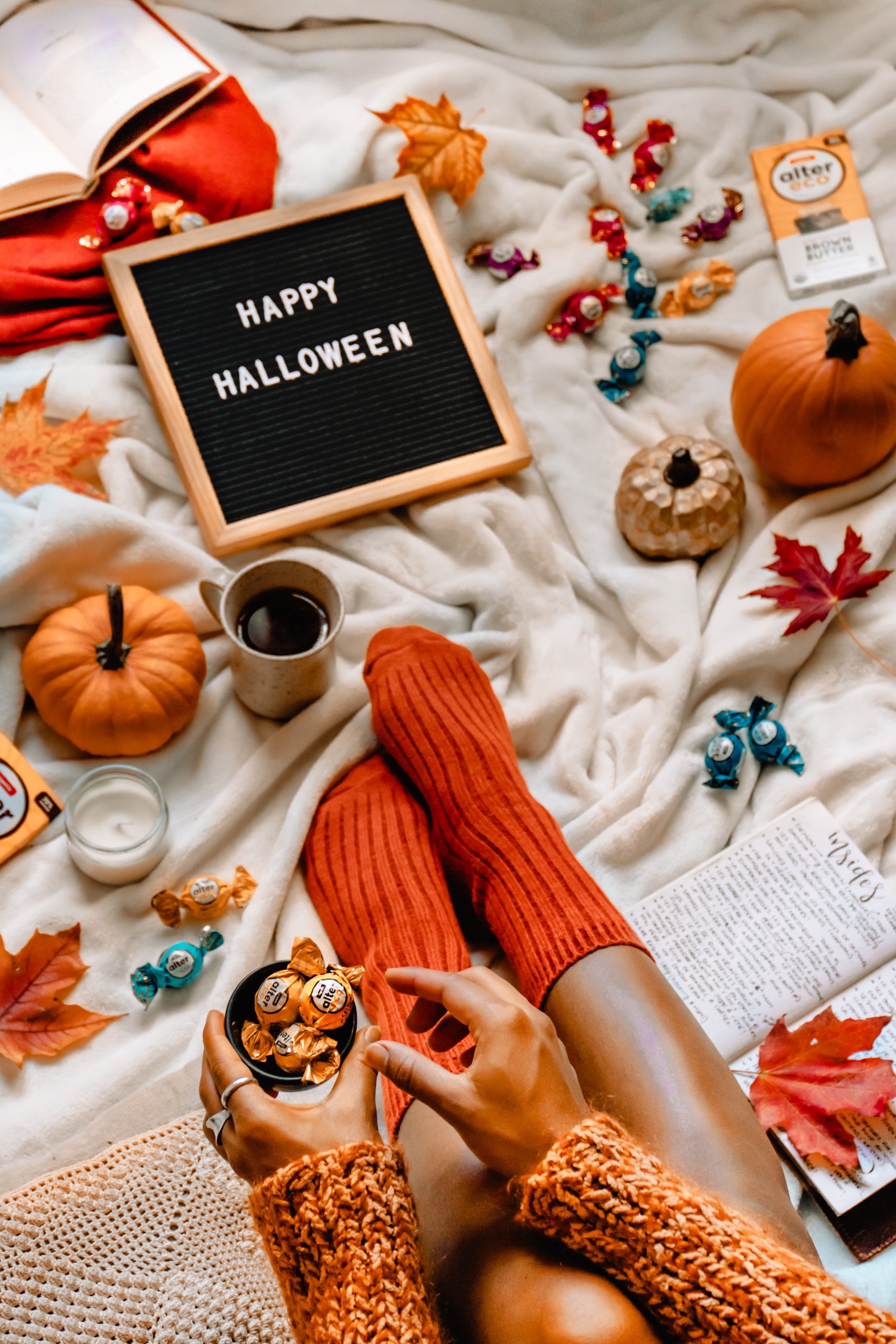 Halloween setup on a blanket with fall leaves, pumpkins and candy