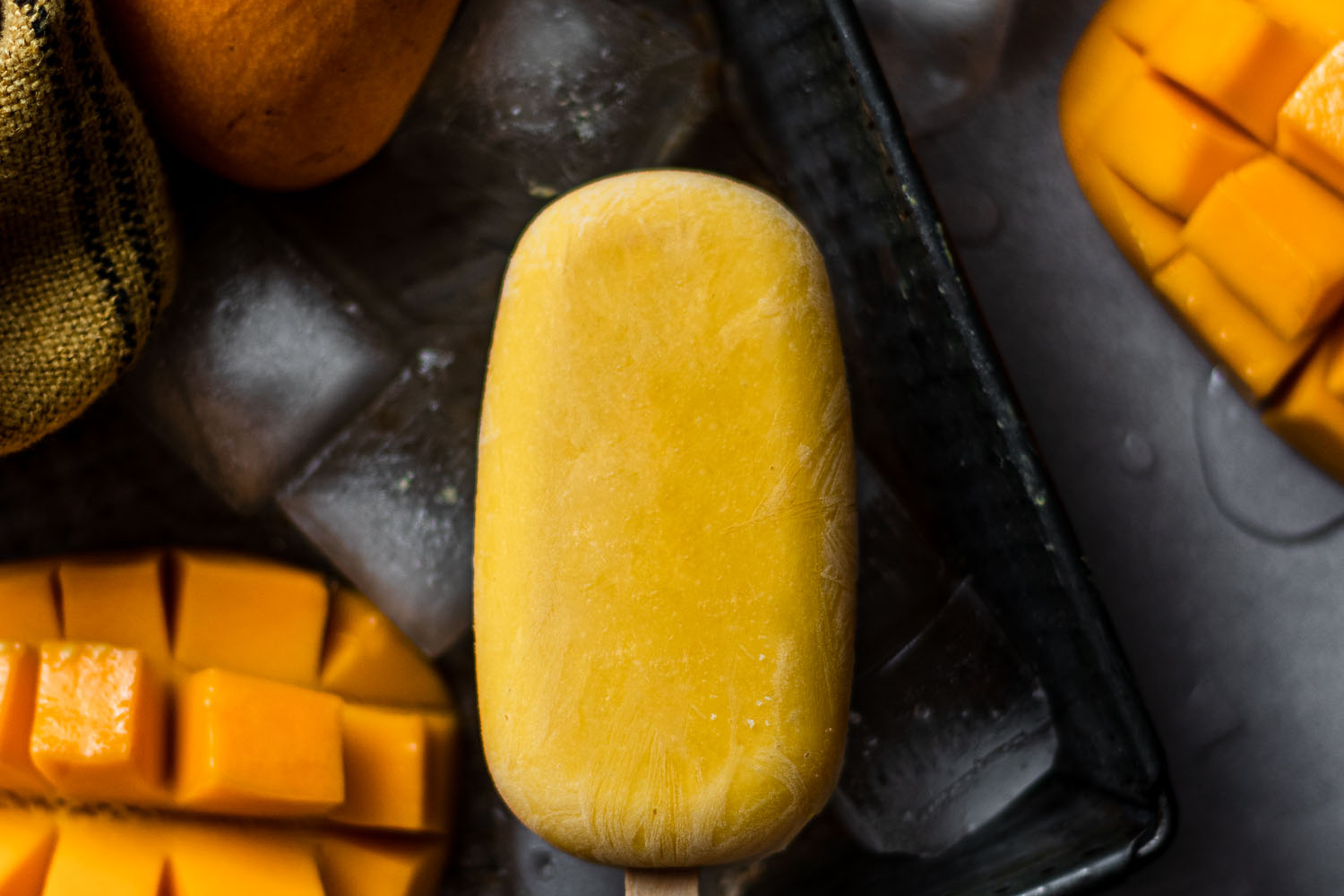 Mango Lassi Pop in a tray with ice and other mangoes.