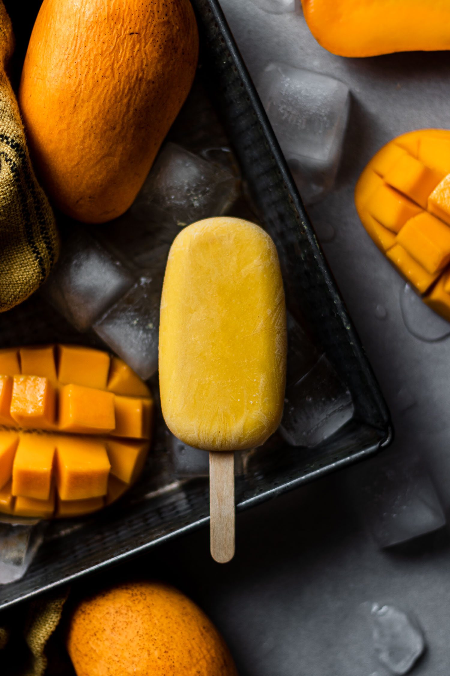 Mango Lassi Pop in a tray with ice and other mangoes.