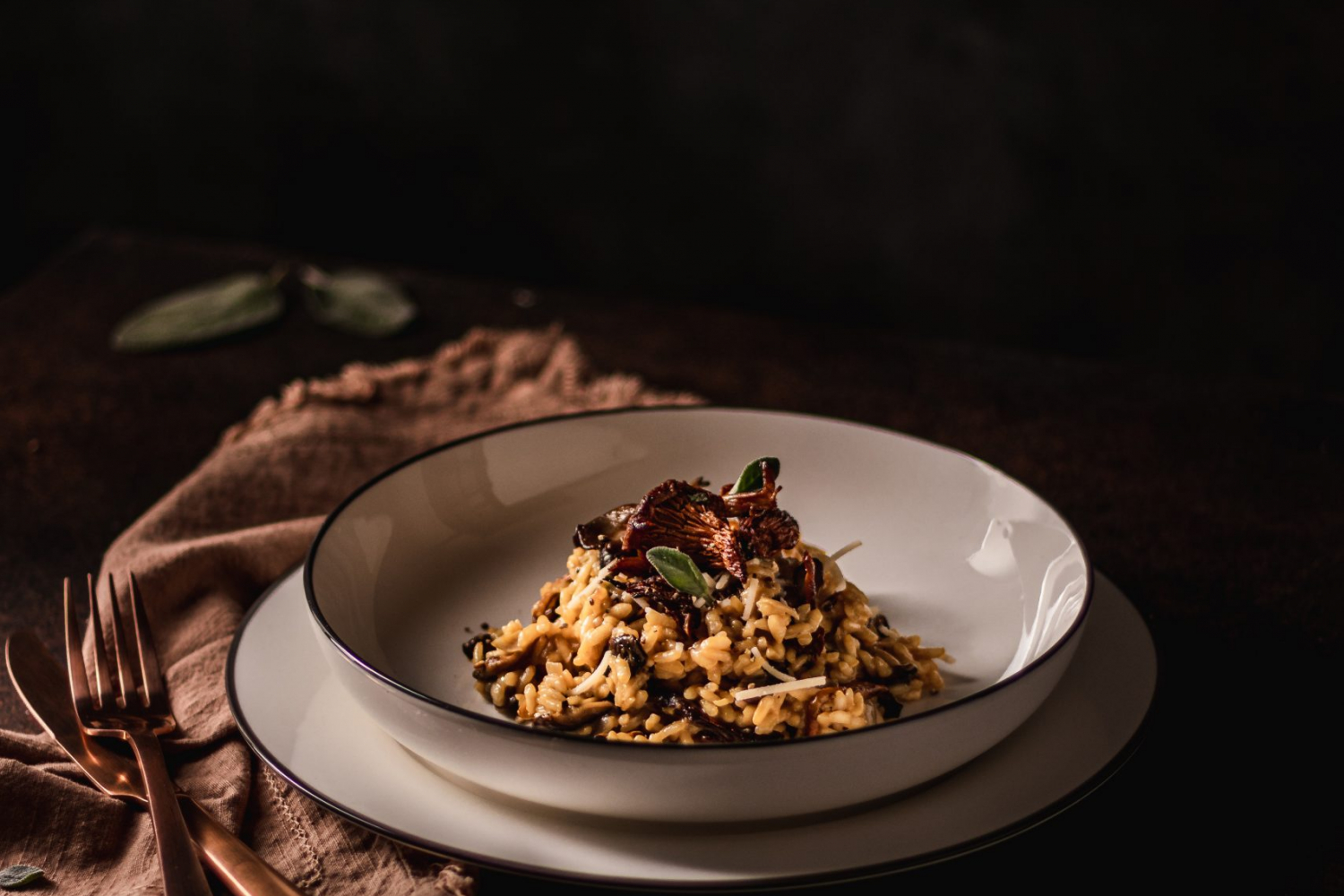 Plate of risotto garnished with cooked wild mushrooms and fresh sage.
