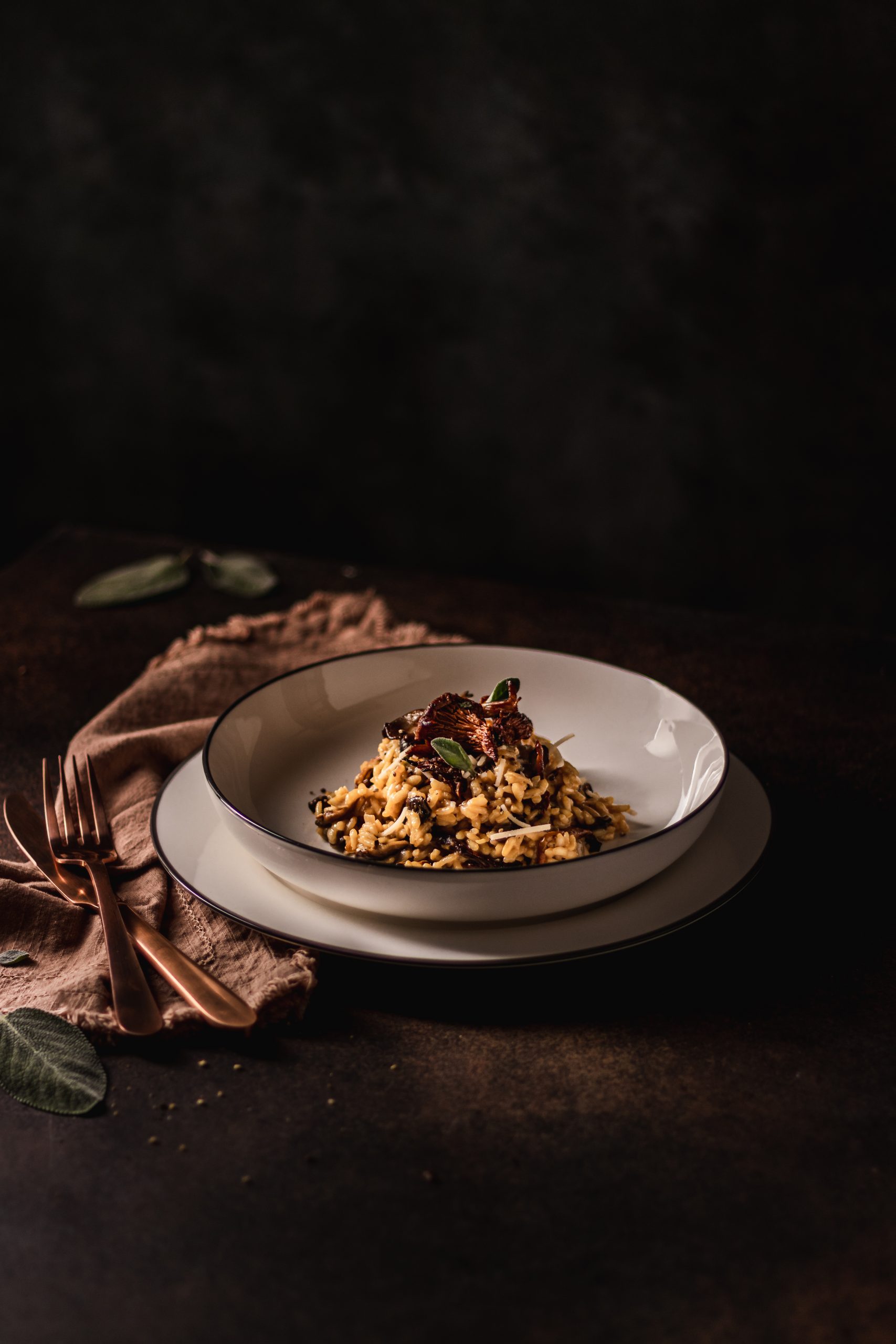 Plate of risotto garnished with cooked wild mushrooms and fresh sage.