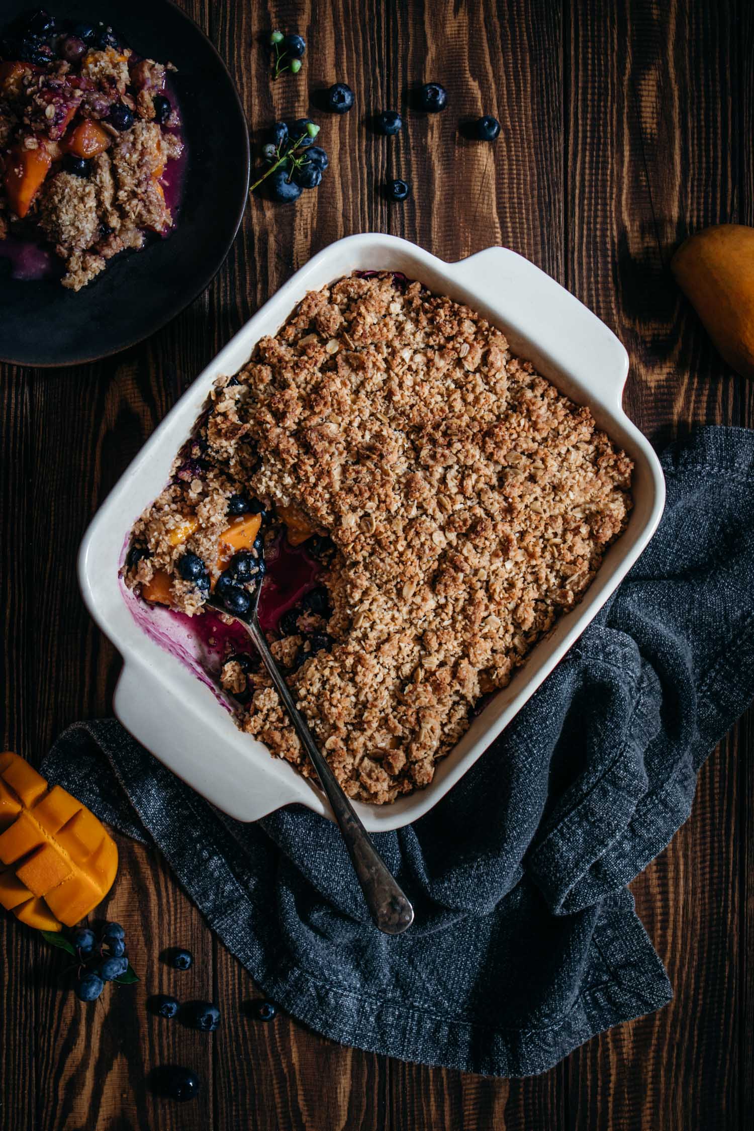 Baked blueberry mango crumble out of the oven with one serving taken out.