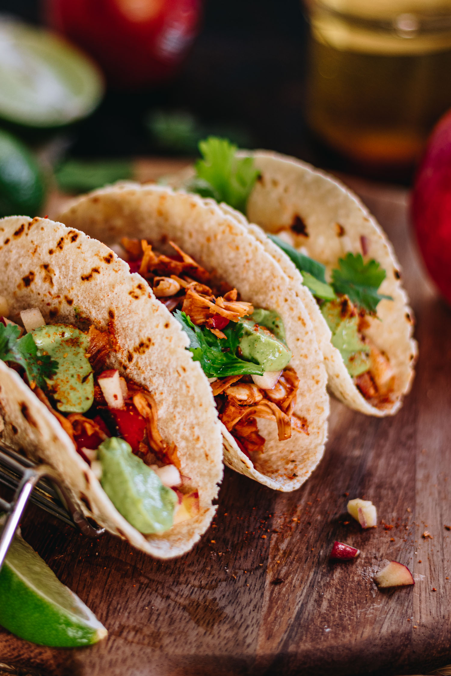 Close up of 3 Tacos in taco rack surrounded by limes, apple salsa, avocado crema and corn tortillas