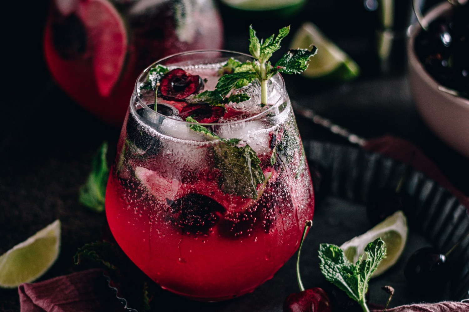Cherry mojito garnished with fresh mint and surrounded by limes