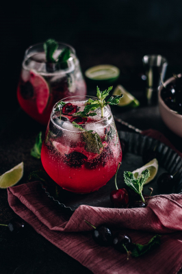 Cherry mojito garnished with fresh mint and surrounded by limes