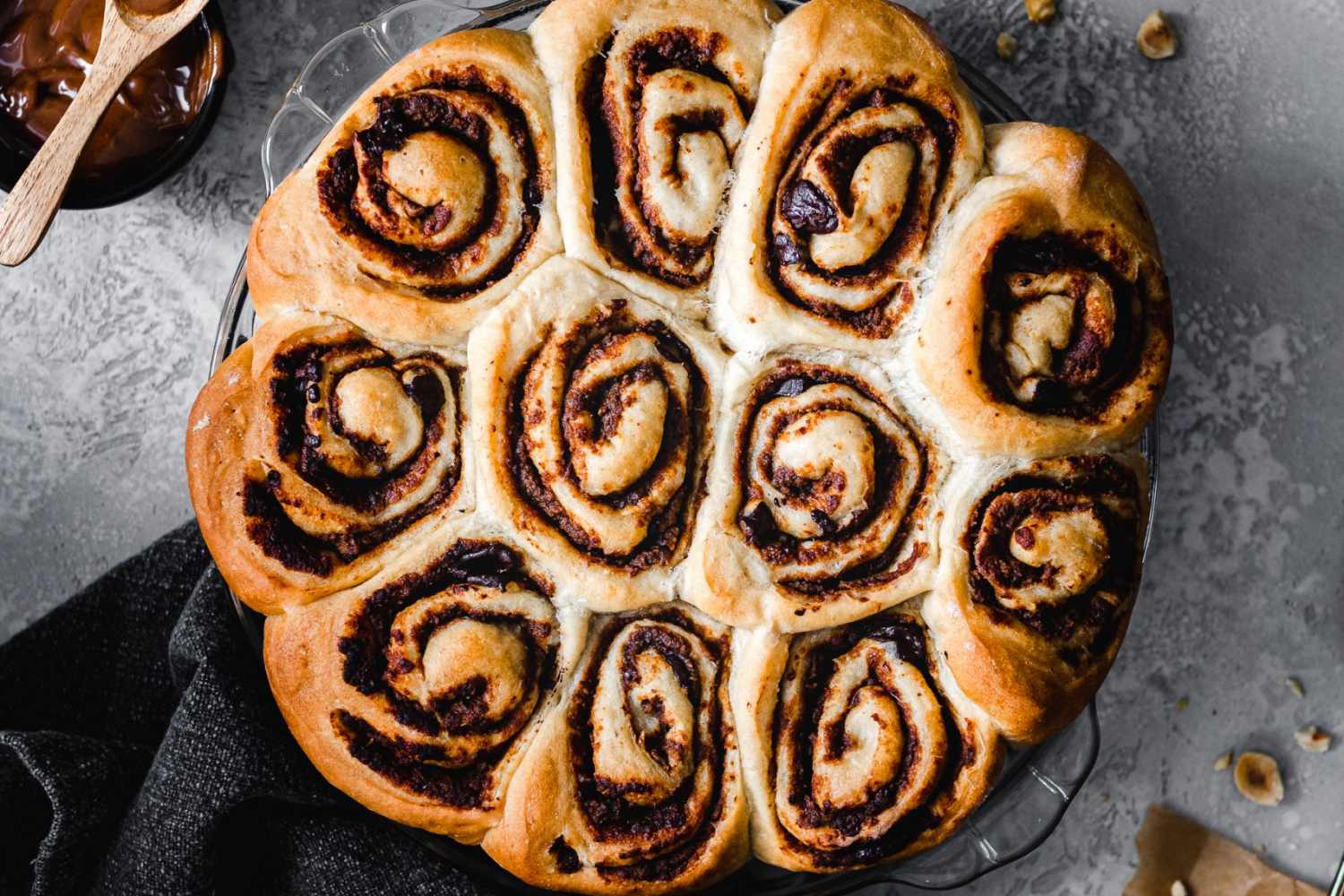 Chocolate hazelnut buns in a pan surrounded by whole hazelnuts