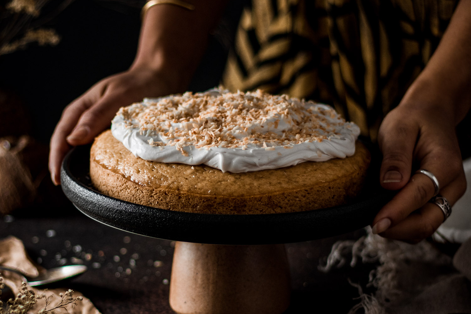 Coconut Cake on a sand surrounded by fresh coconuts and dried toasted coconut