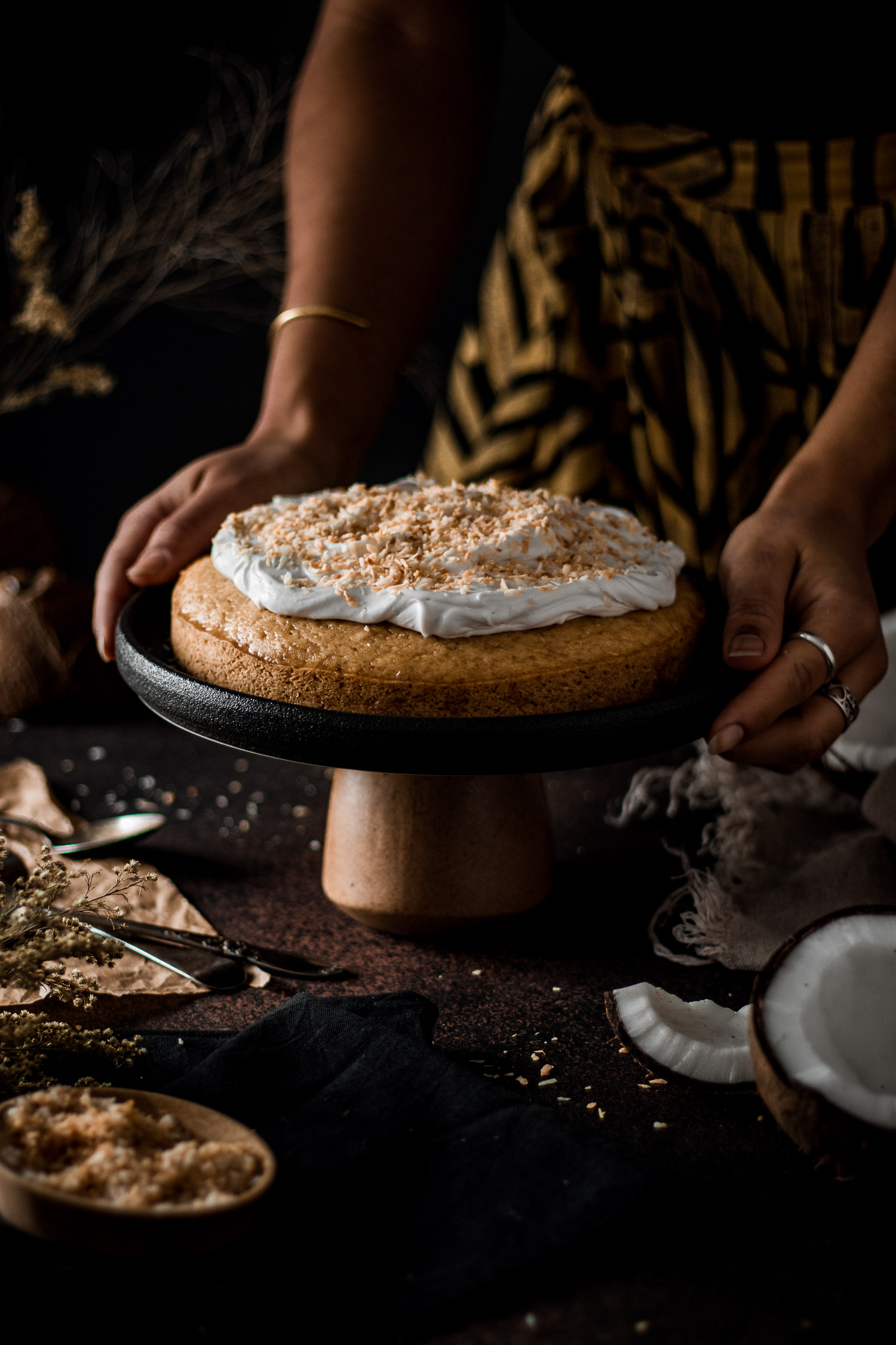 Coconut Cake on a sand surrounded by fresh coconuts and dried toasted coconut
