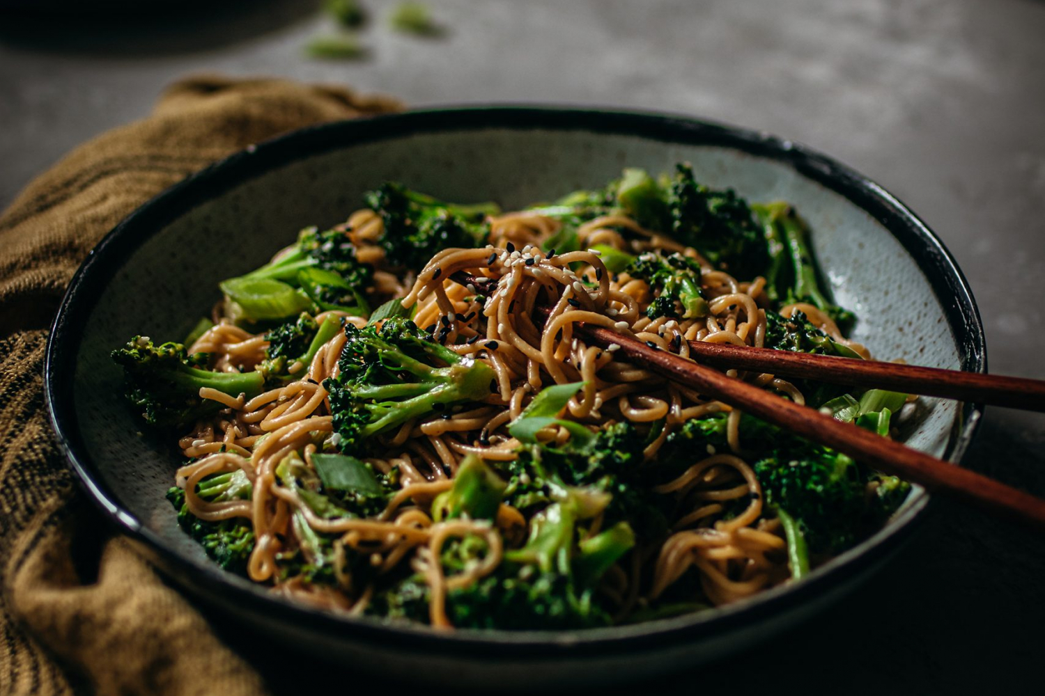 Creamy Sesame and Broccoli Noodles with chopsticks in bowl touching the noodles