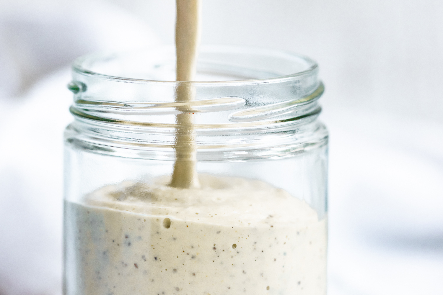 Creamy cashew dressing being poured into a jar