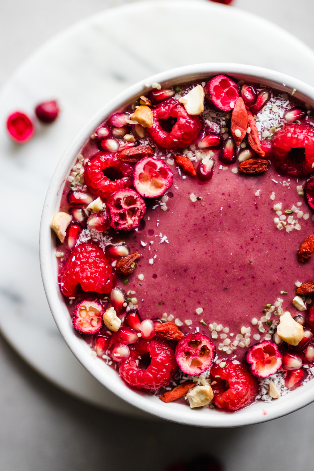 Closeup of Ruby Red Smoothie Bowl in a bowl topped with raspberries, pomegranates, cranberries, and hemp hearts