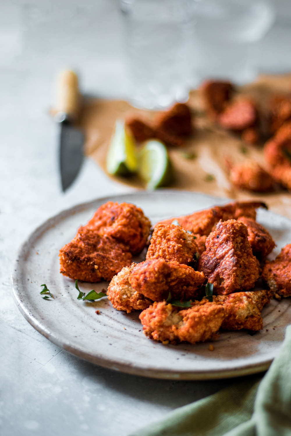 Panko crusted cauliflower on a plate with limes in the background and other panko crusted vegan wings