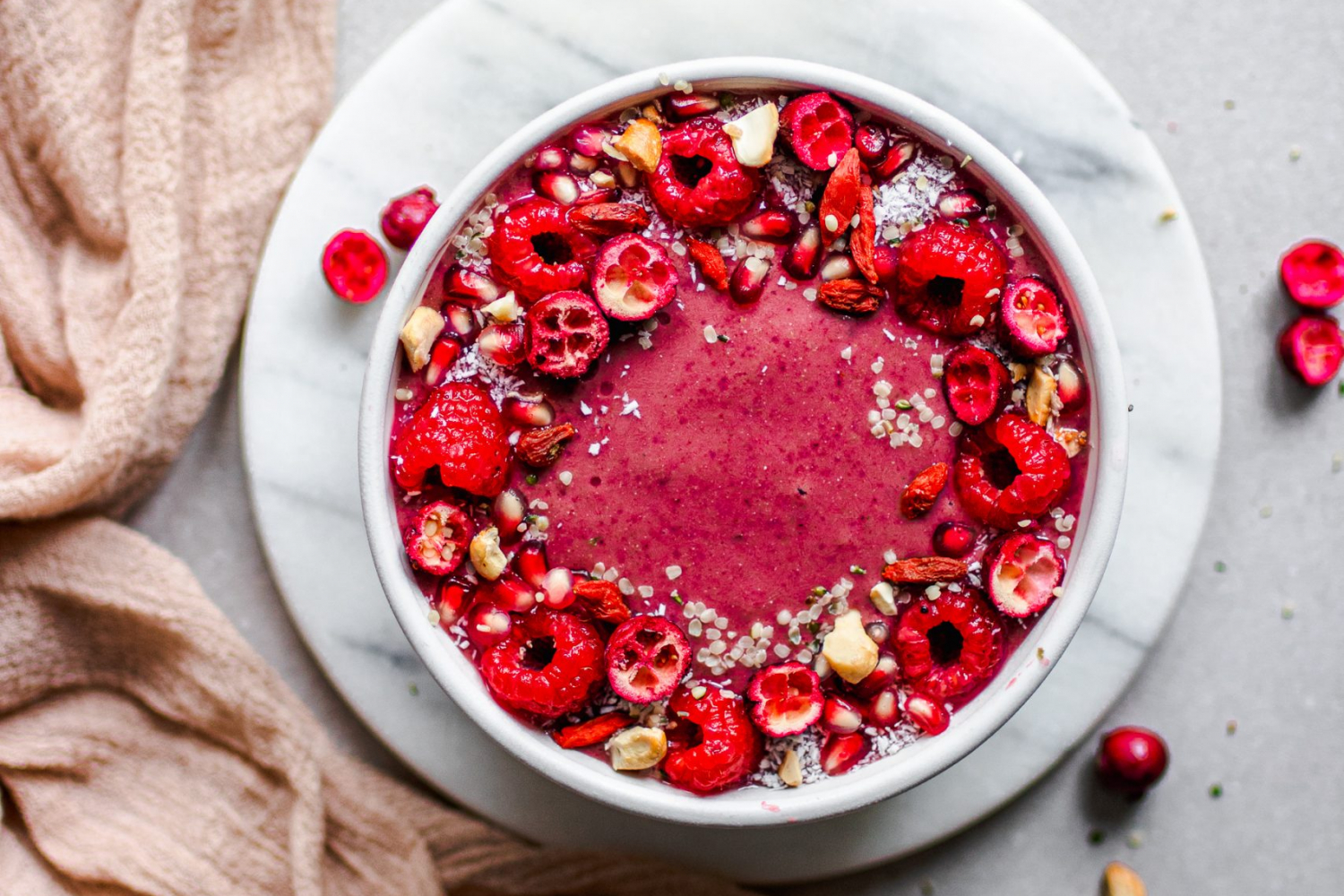 Red smoothie bowl topped with cashews, raspberries, cashews, and cranberries