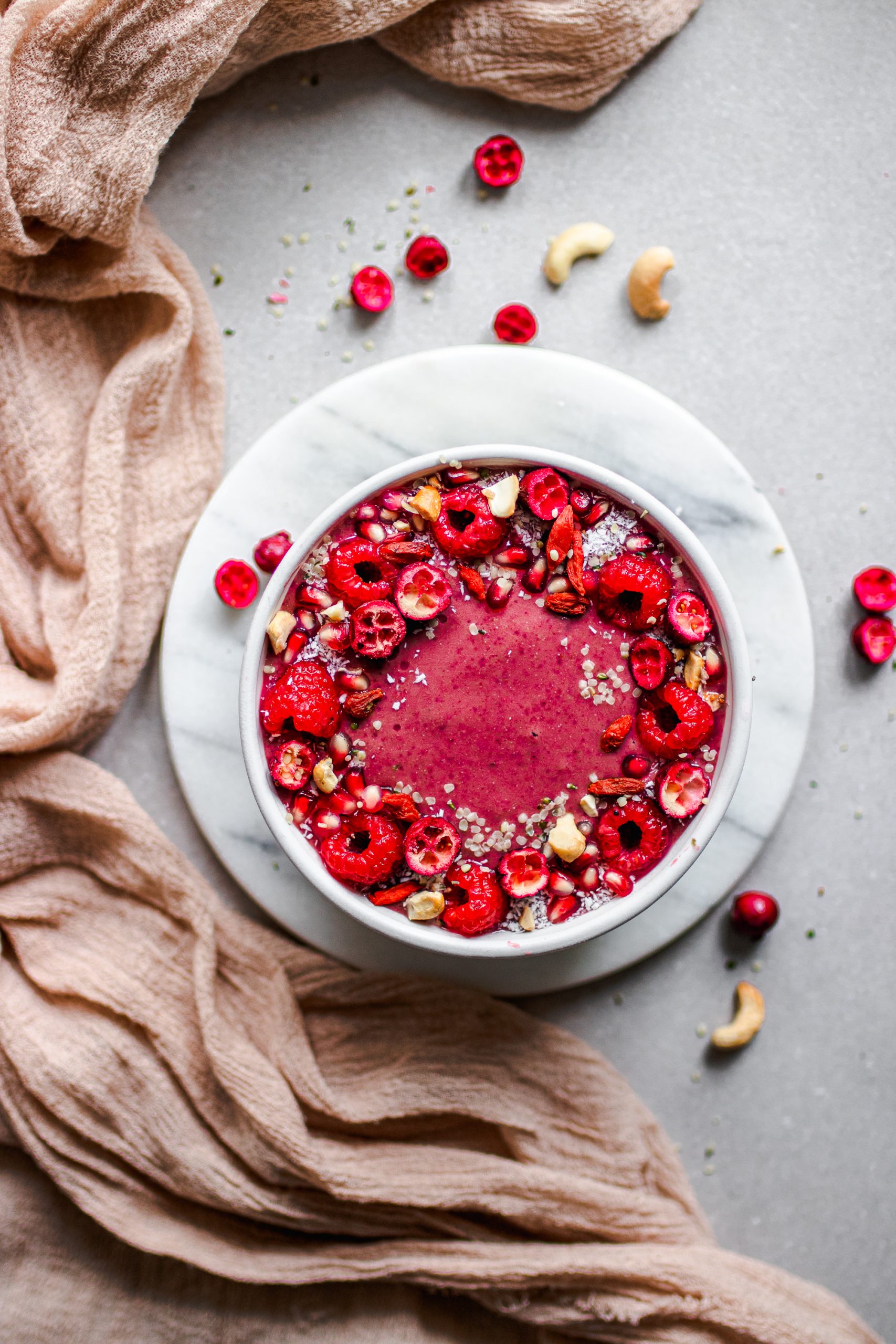 Red smoothie bowl topped with cashews, raspberries, cashews, and cranberries