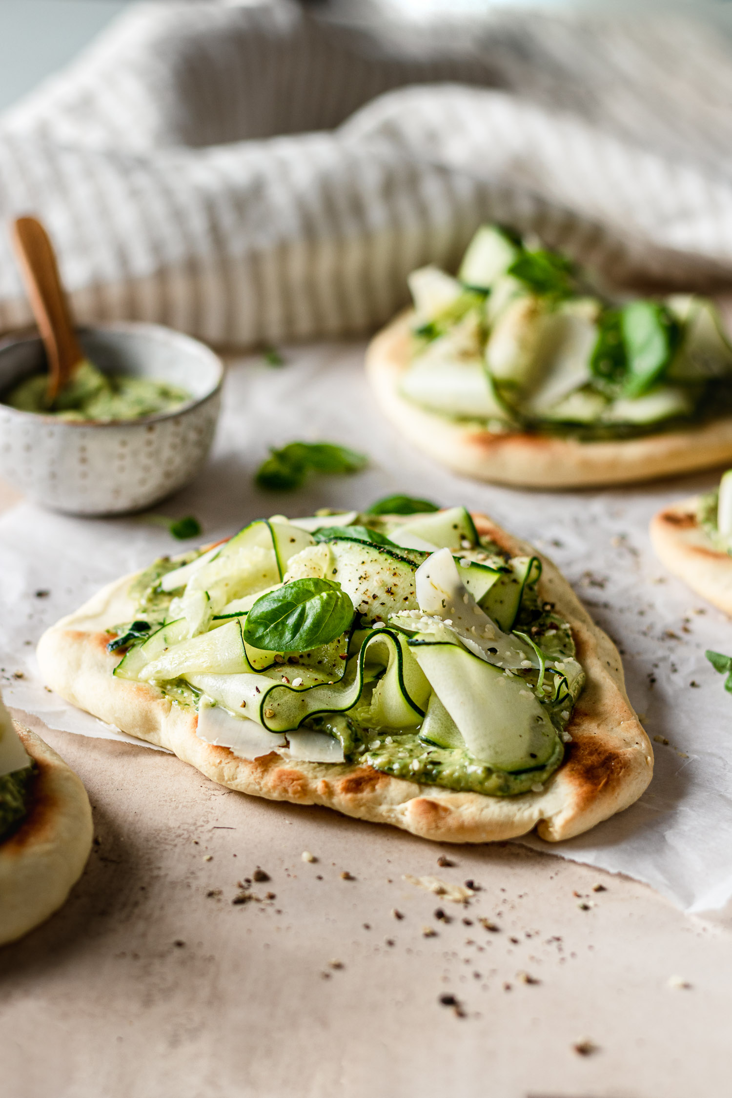 Flatbreads laid flat topped with roasted garlic pesto, shaved zucchini, and fresh basil.
