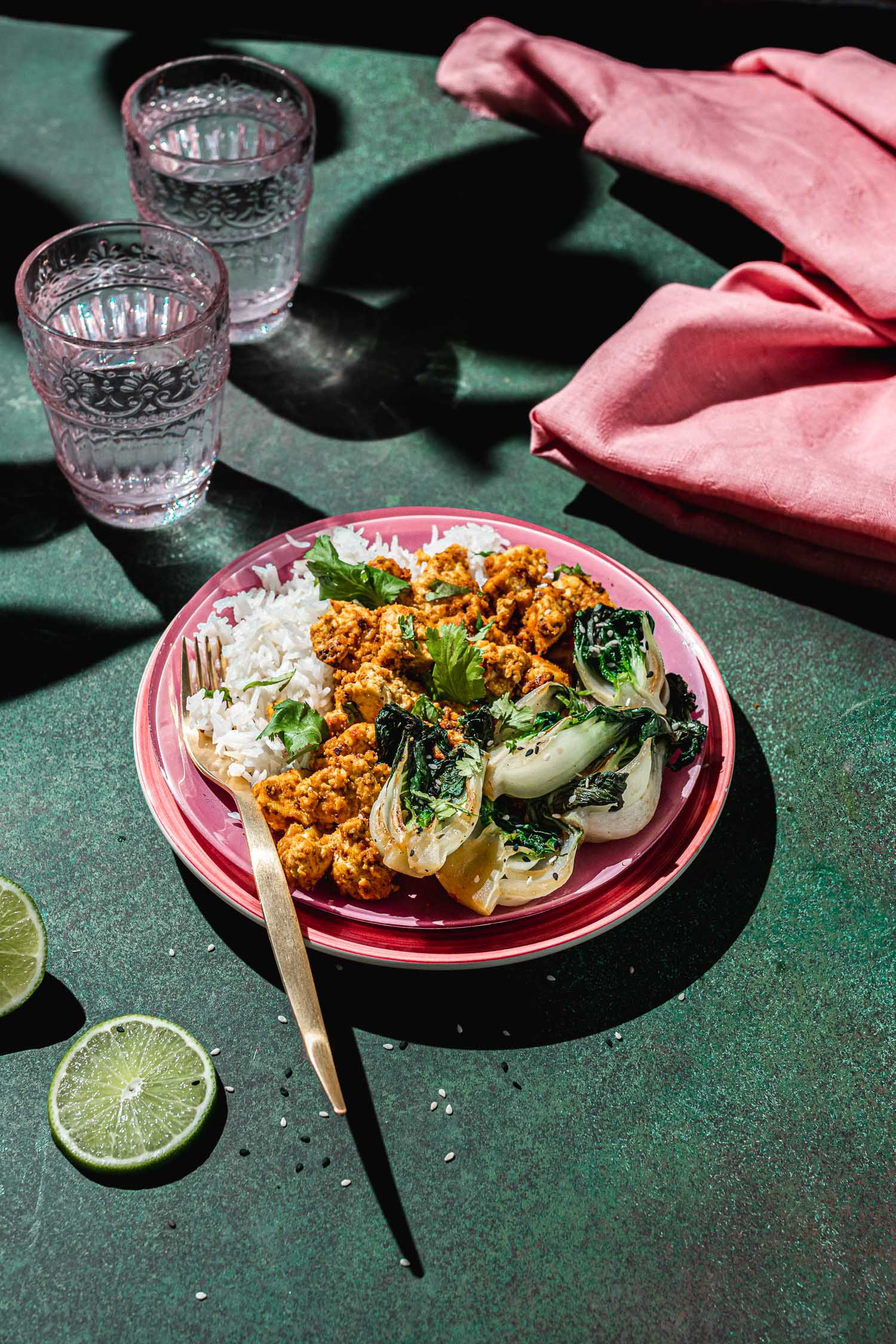 Plate of nutritional yeast coated tofu with rice and bok choy on a green backdrop.