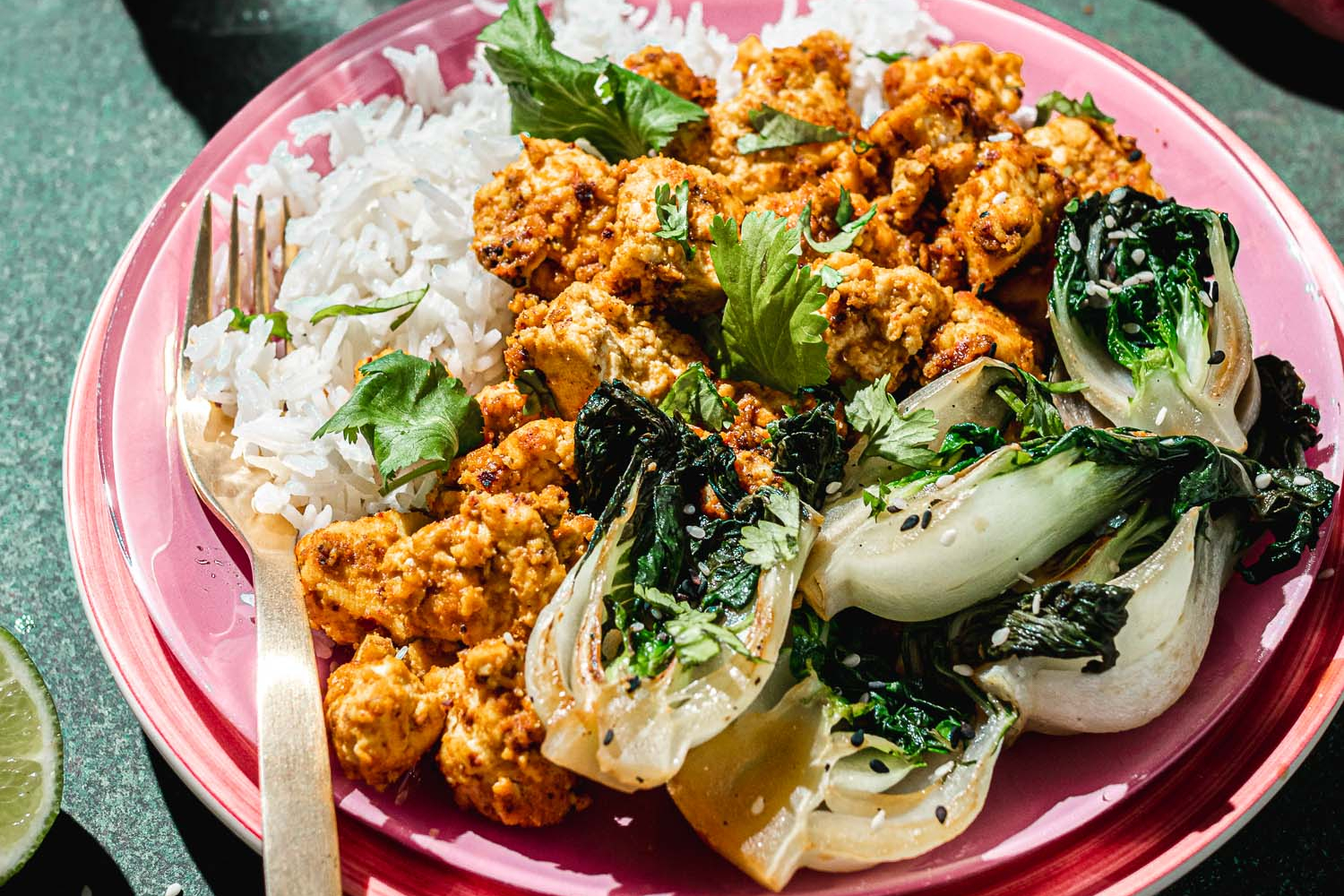 Sweet and spicy tofu in a plink plate served with rice and bok choy.