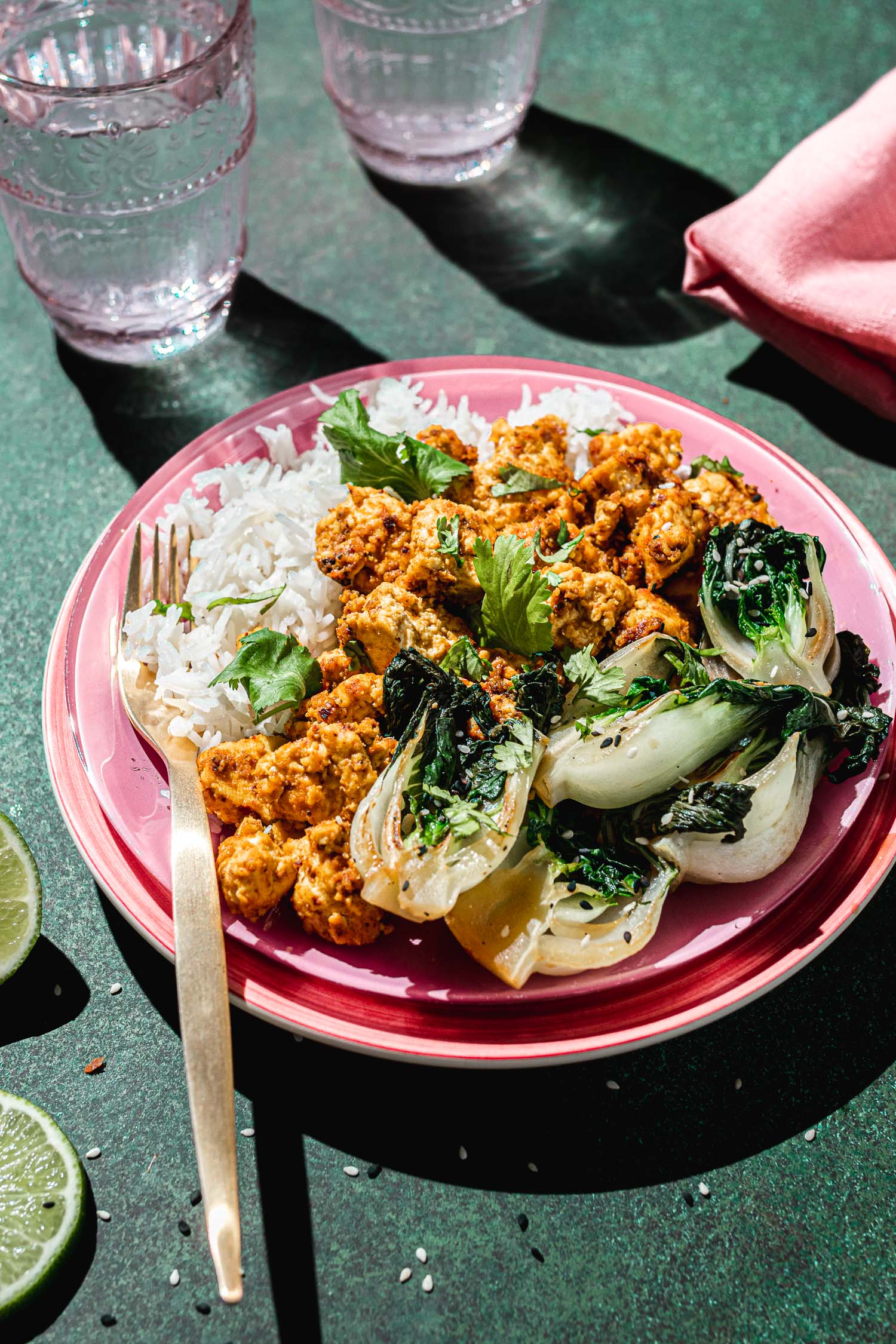 Sweet and spicy tofu in a plink plate served with rice and bok choy.