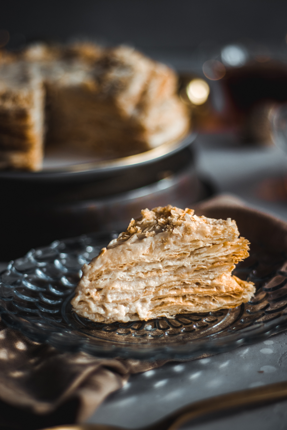 Slice of napoleon cake on glass plate with full cake in the background