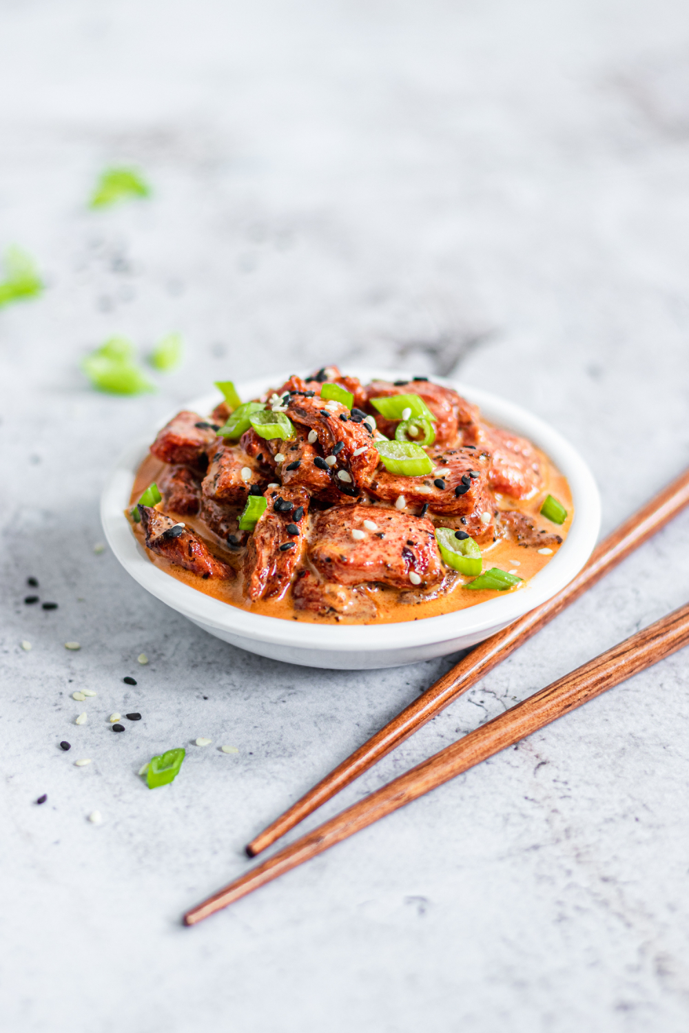 Vegan watermelon tuna in a small bowl with chopsticks next to it. Garnished with sesame seeds and green onions