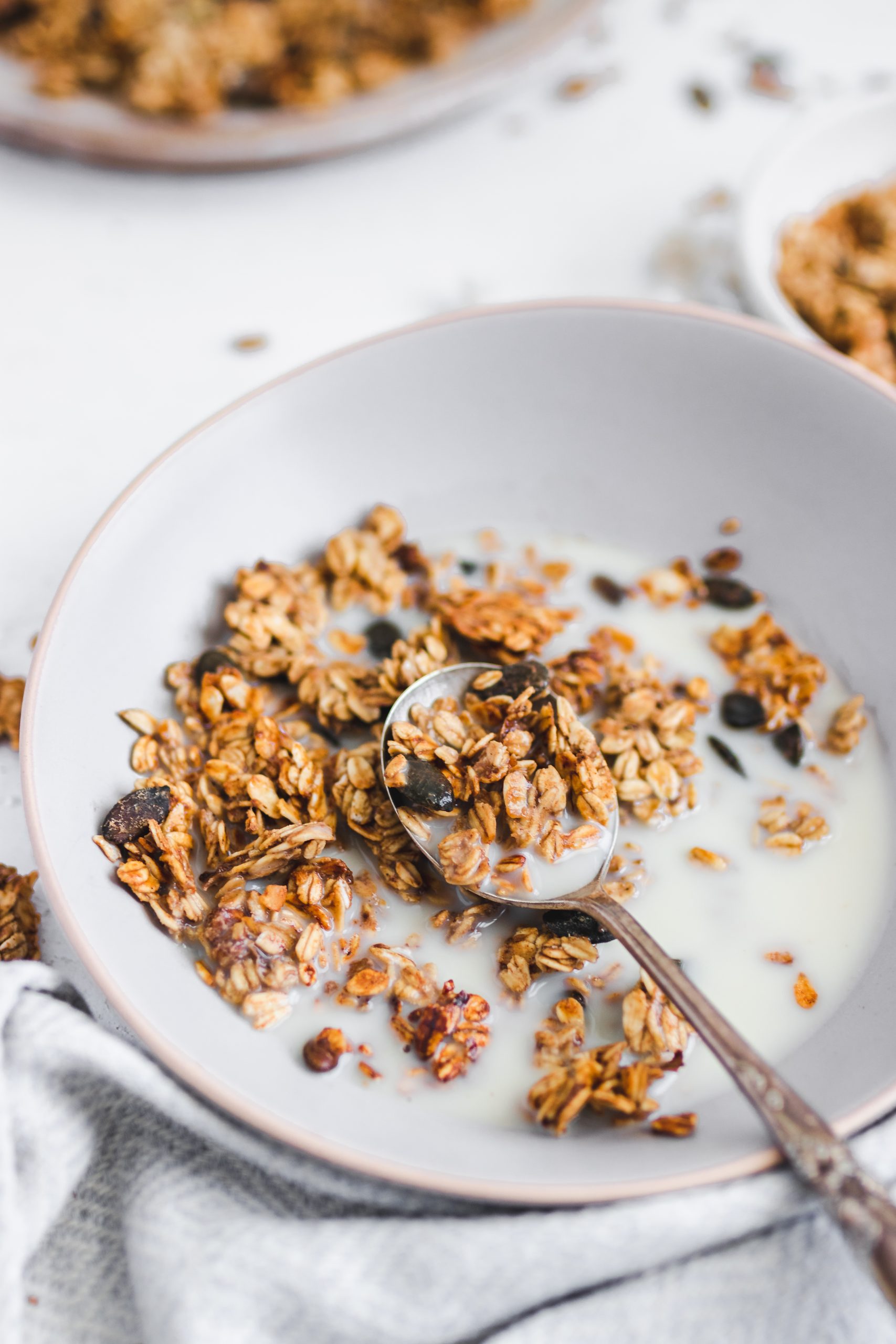 Oil Free Peanut Butter and Banana Granola in a bowl with milk, spoon taken out