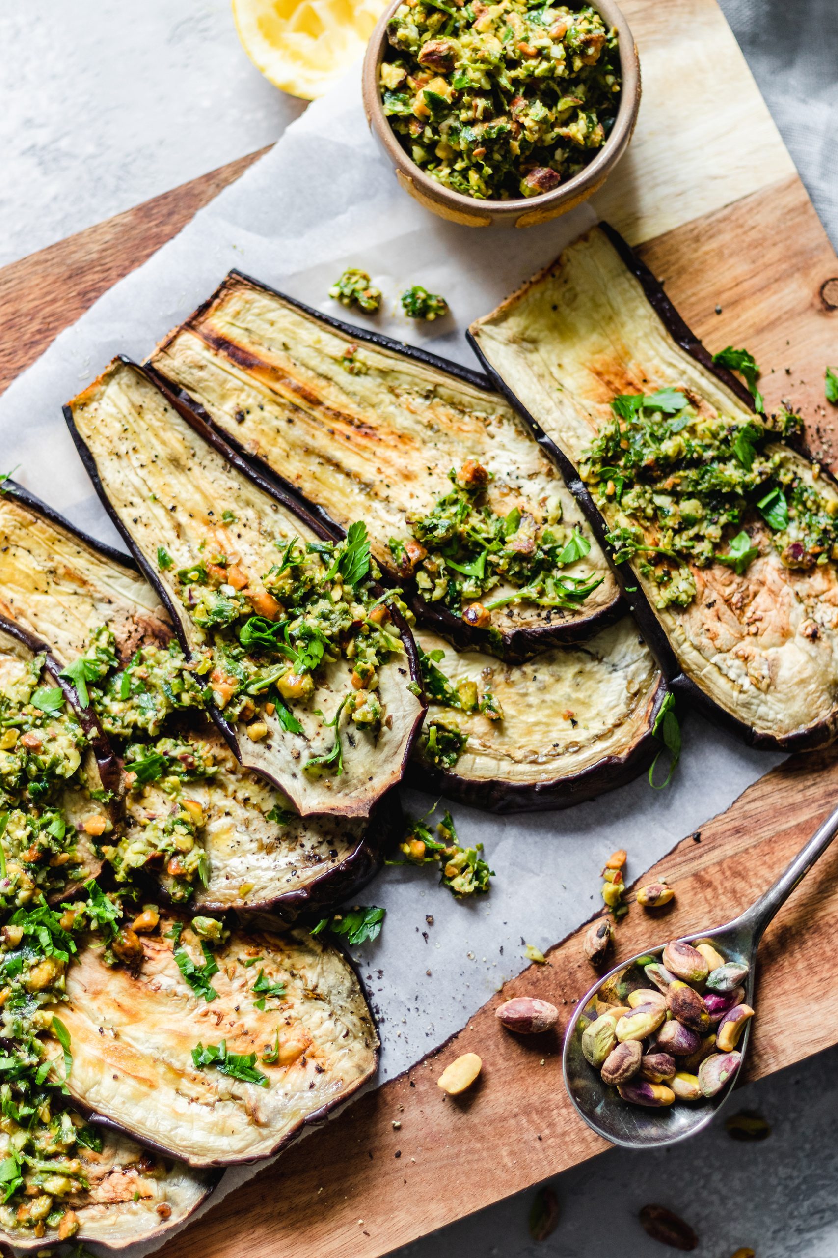 Sliced eggplants on a cutting board, topped with pistachio gremolata