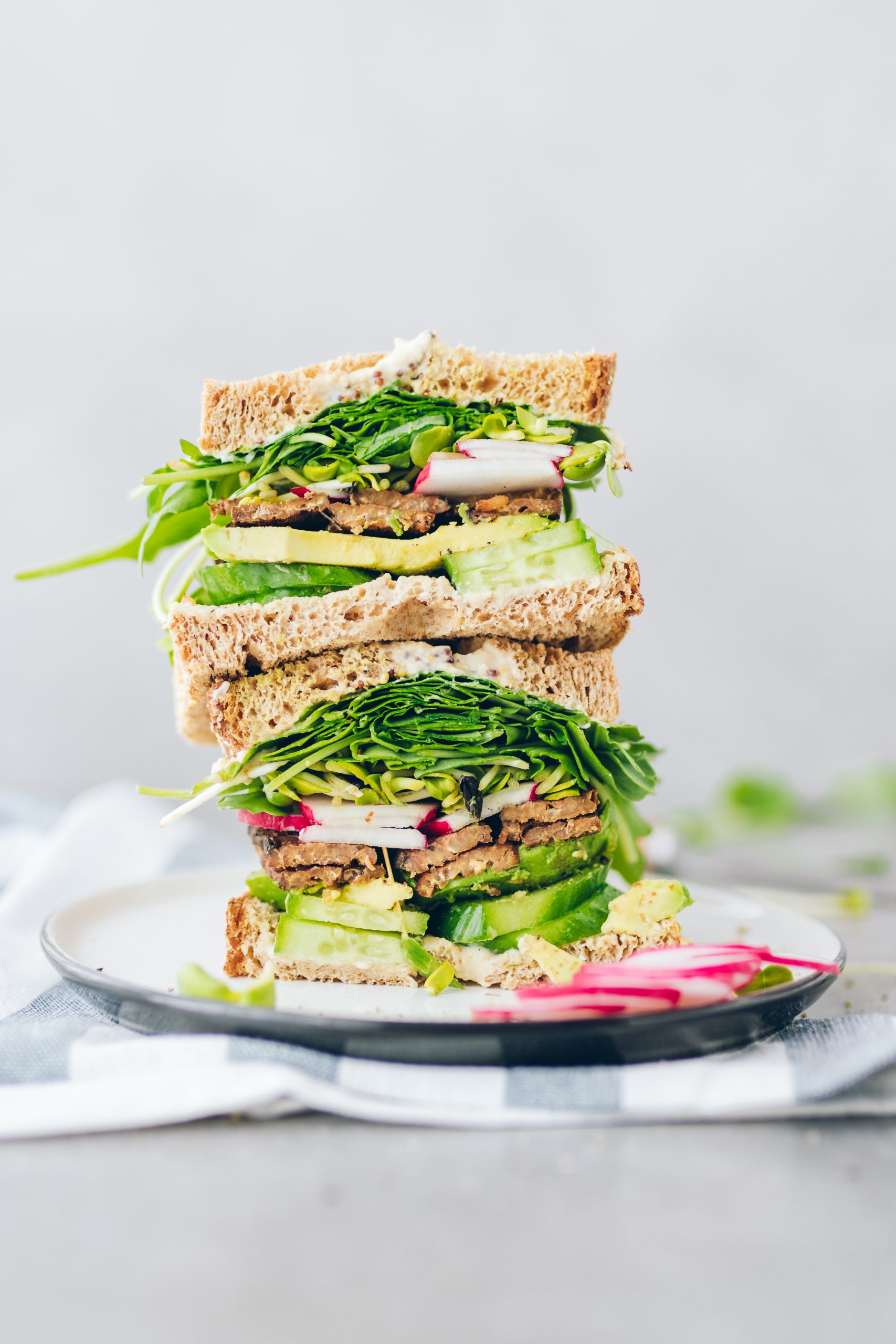 Spring Sandwich with Tempeh Bacon, Arugula and Broccoli Sprouts cut in half and stacked on top of each other