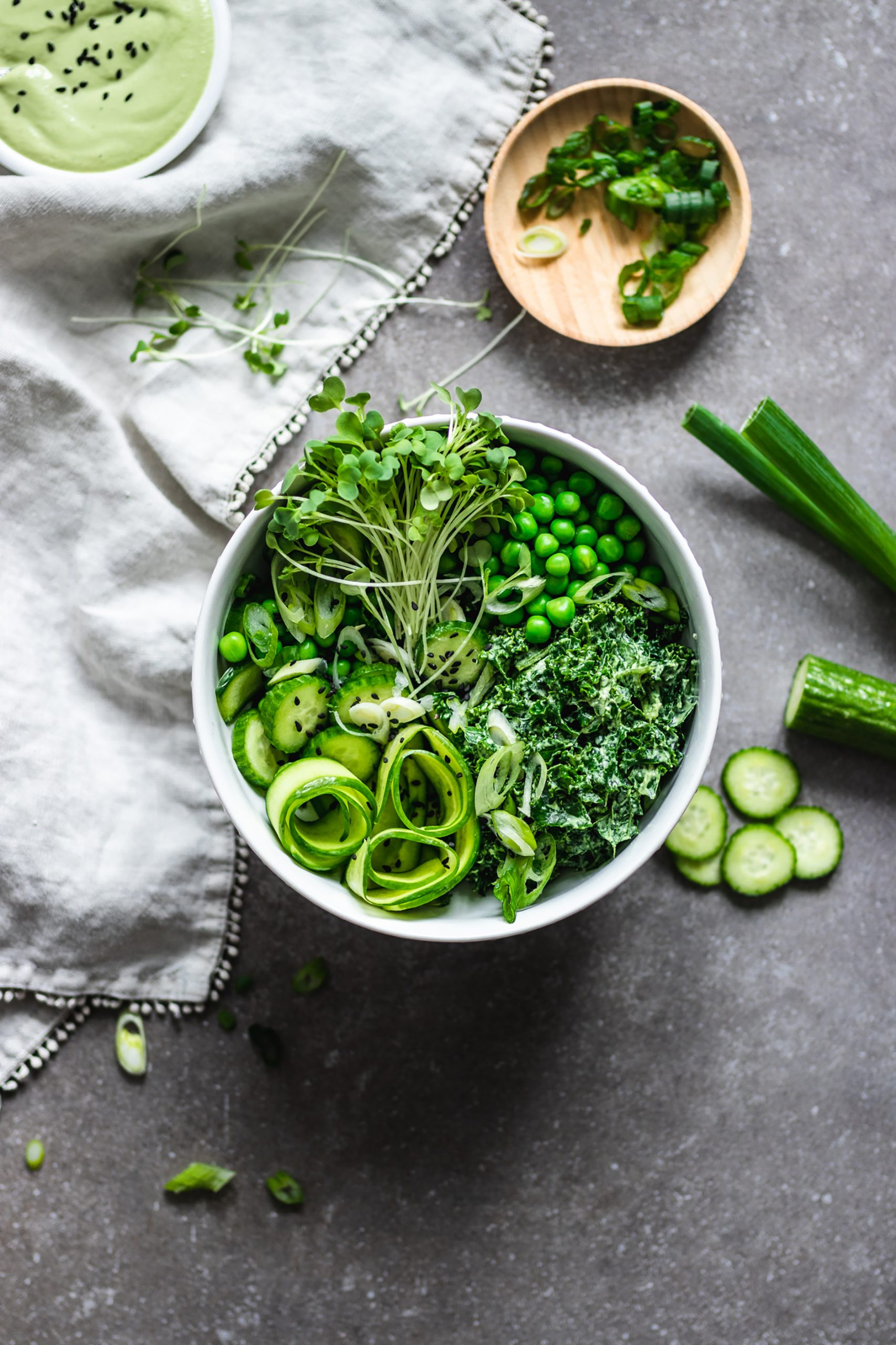 Green Goddess Salad with Cashew Basil Dressing surrounded by cucumbers, green onions and sprouts