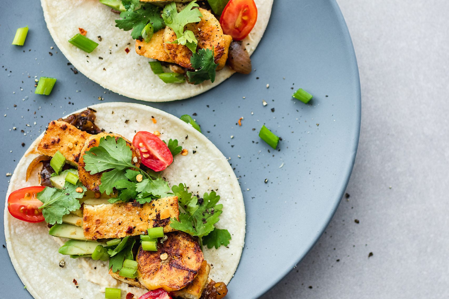Marinated Tofu Tacos on plate garnished with cherry tomatoes and plantains