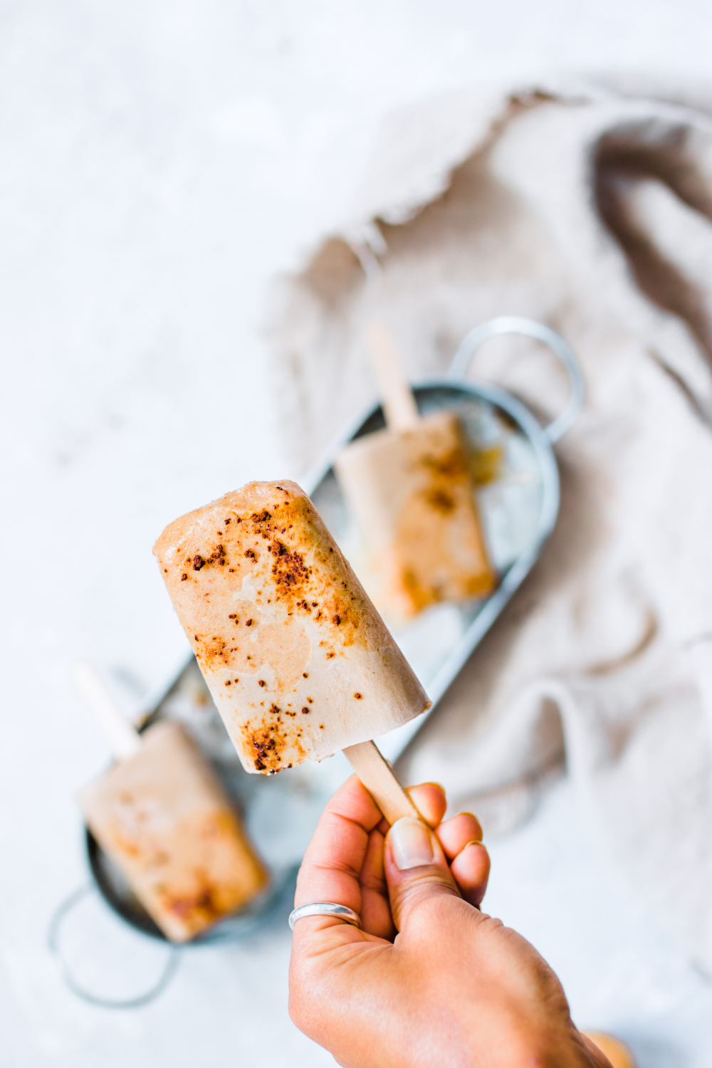 Salted Caramel Latte Pops in a tray with ice and one pop is held by a hand
