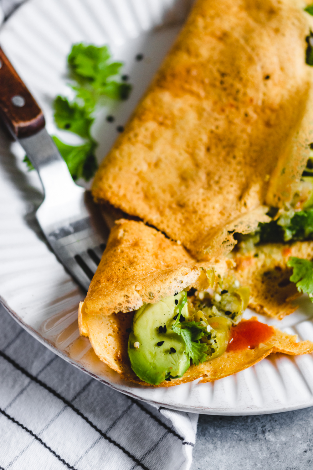 Savoury Flour Chickpea Crepes served with herbs, avocado, and hot sauce