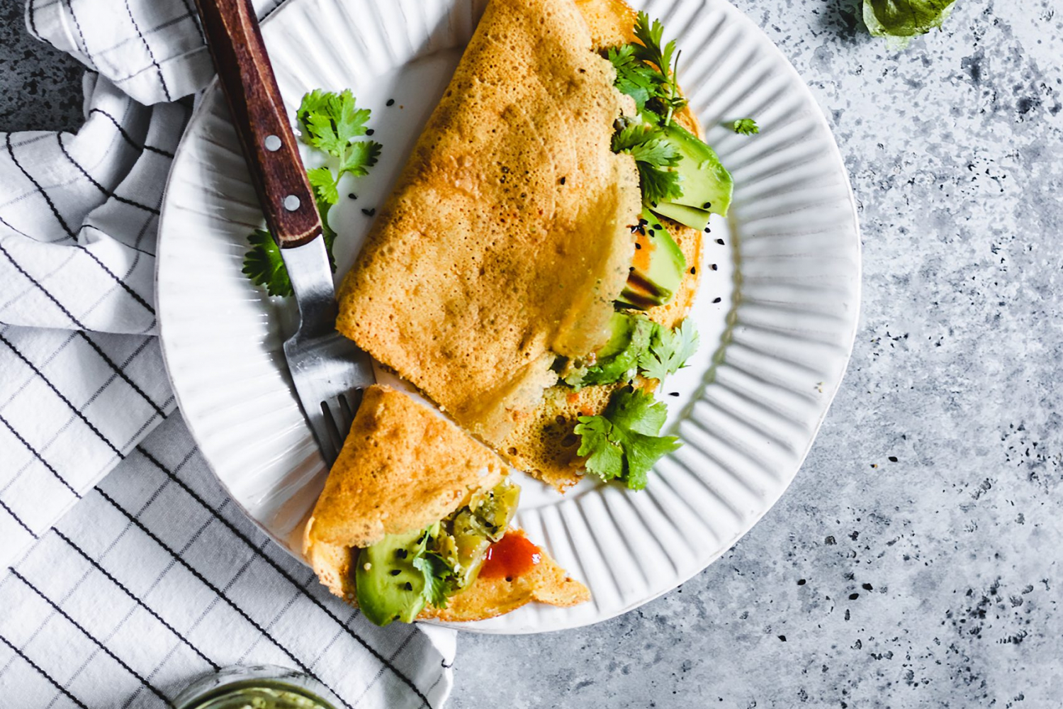 Savoury Flour Chickpea Crepes served with herbs, avocado, and hot sauce