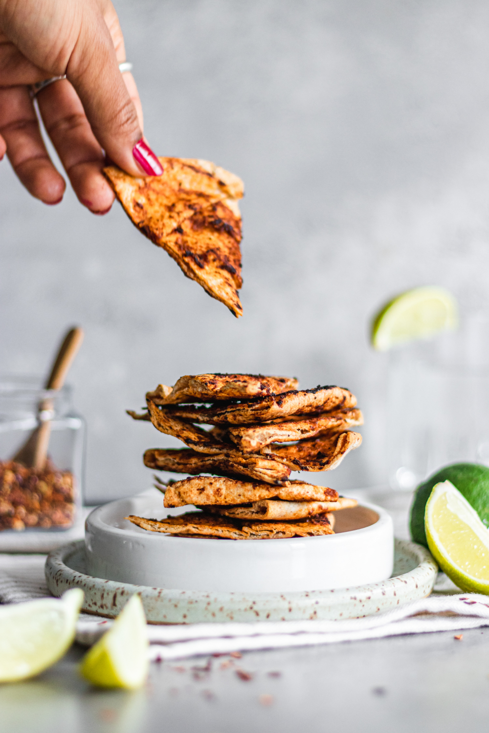 Stack of Whole Wheat Chili and Lime Pita Chips on a plate with hand reaching for one