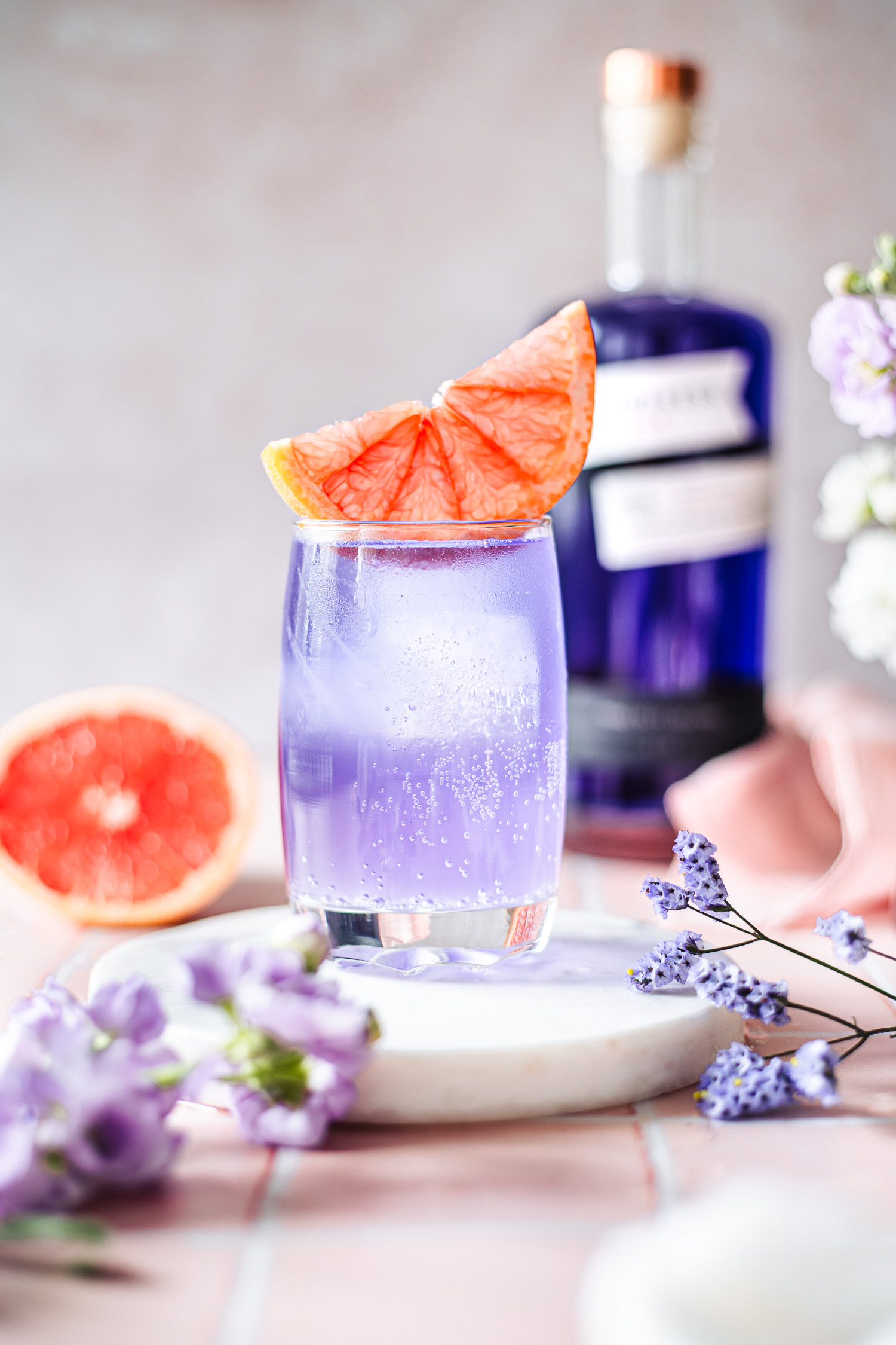 Elderflower Gin Fizz with a slice of pink grapefruit with a bottle of Empress 1908 Gin in the background.