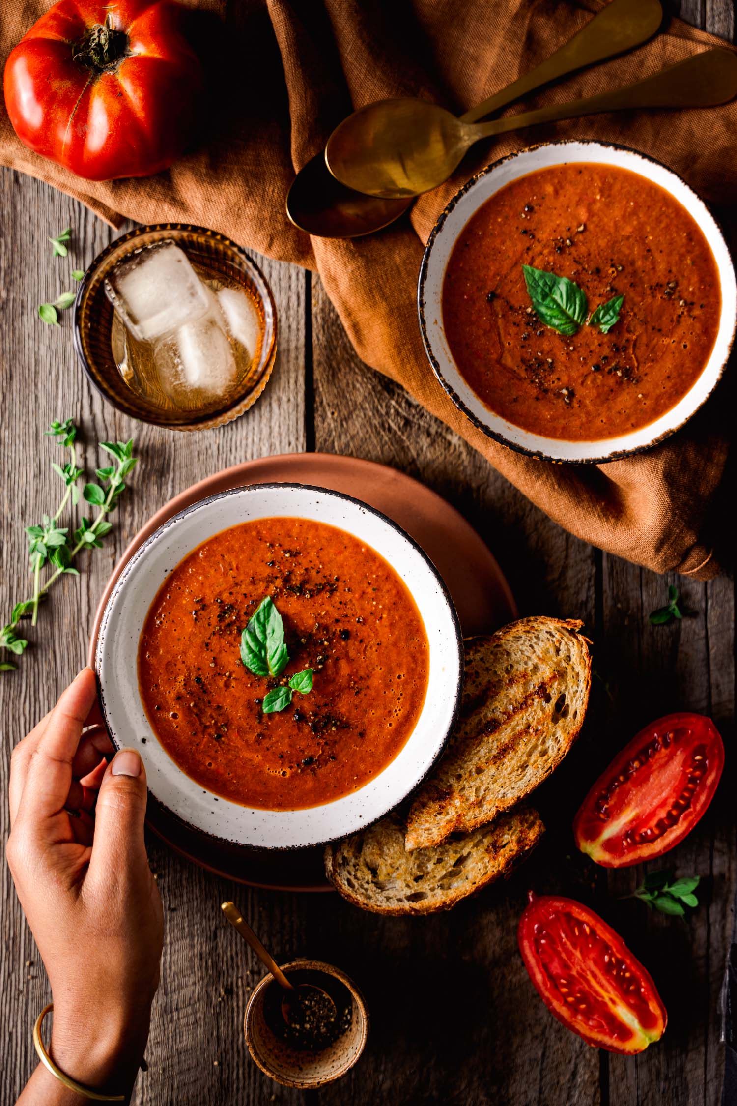 Overhead of Roasted Tomato and Bell Pepper Soup with hand touching the bowl.