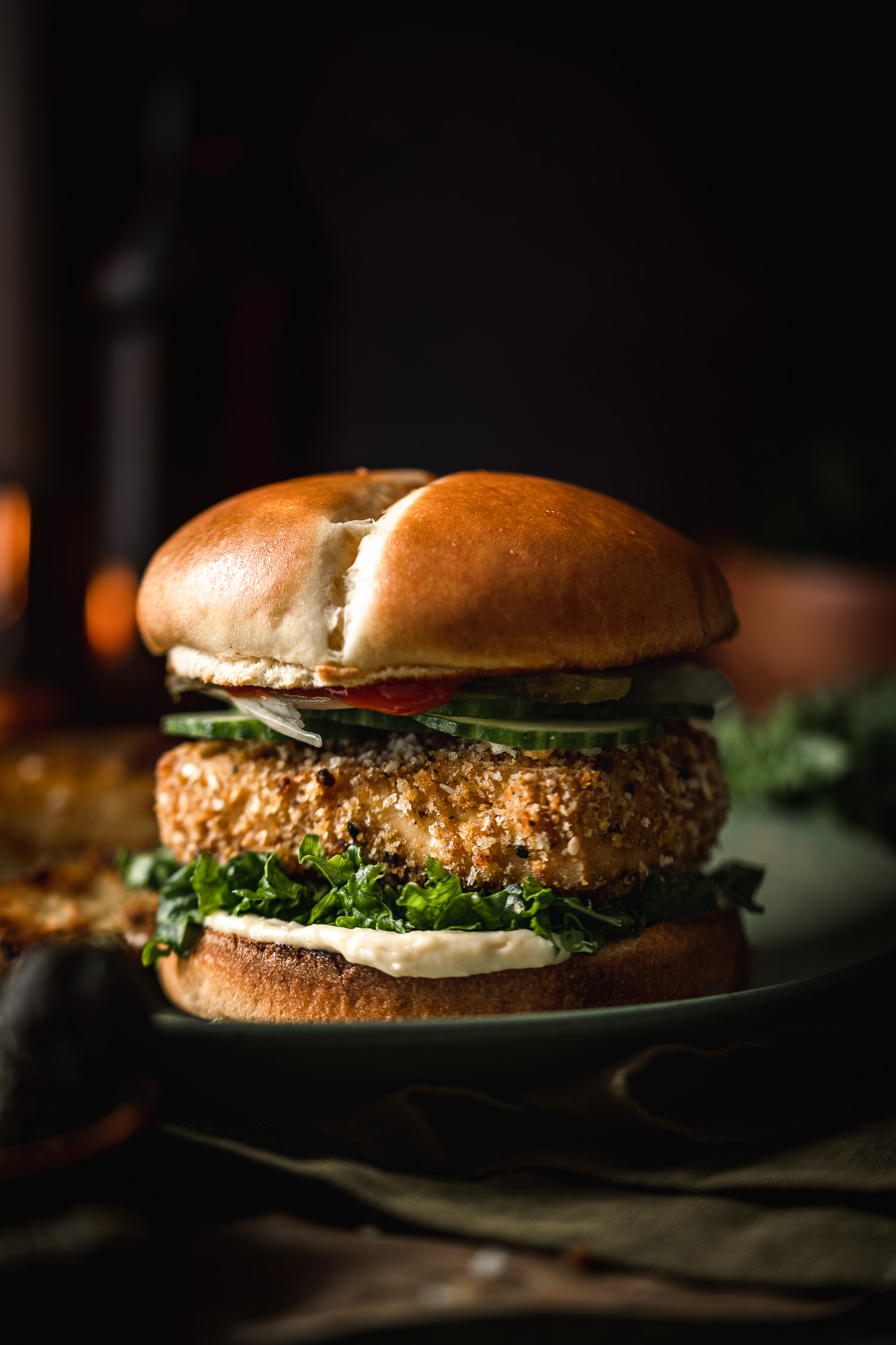 Panko Crusted Tofu Burger with Truffle Massaged Kale on a plate with candlelight in the background
