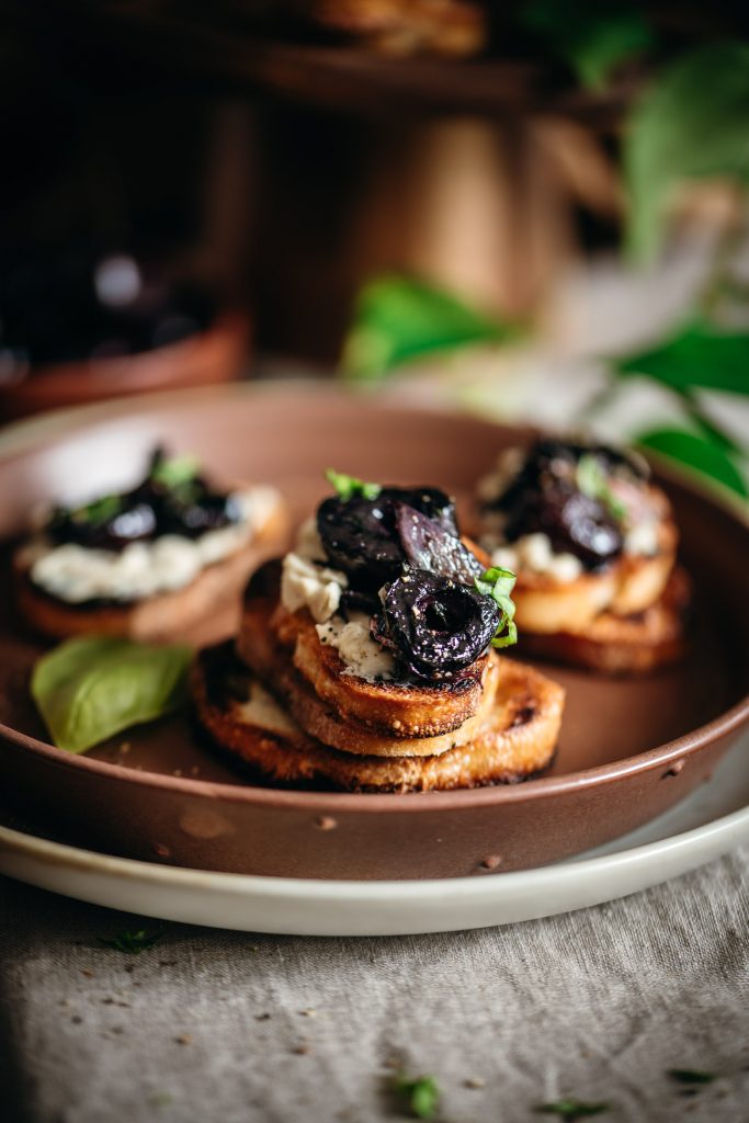 Crostini on a plate topped with vegan cheese, roasted cherries and fresh basil
