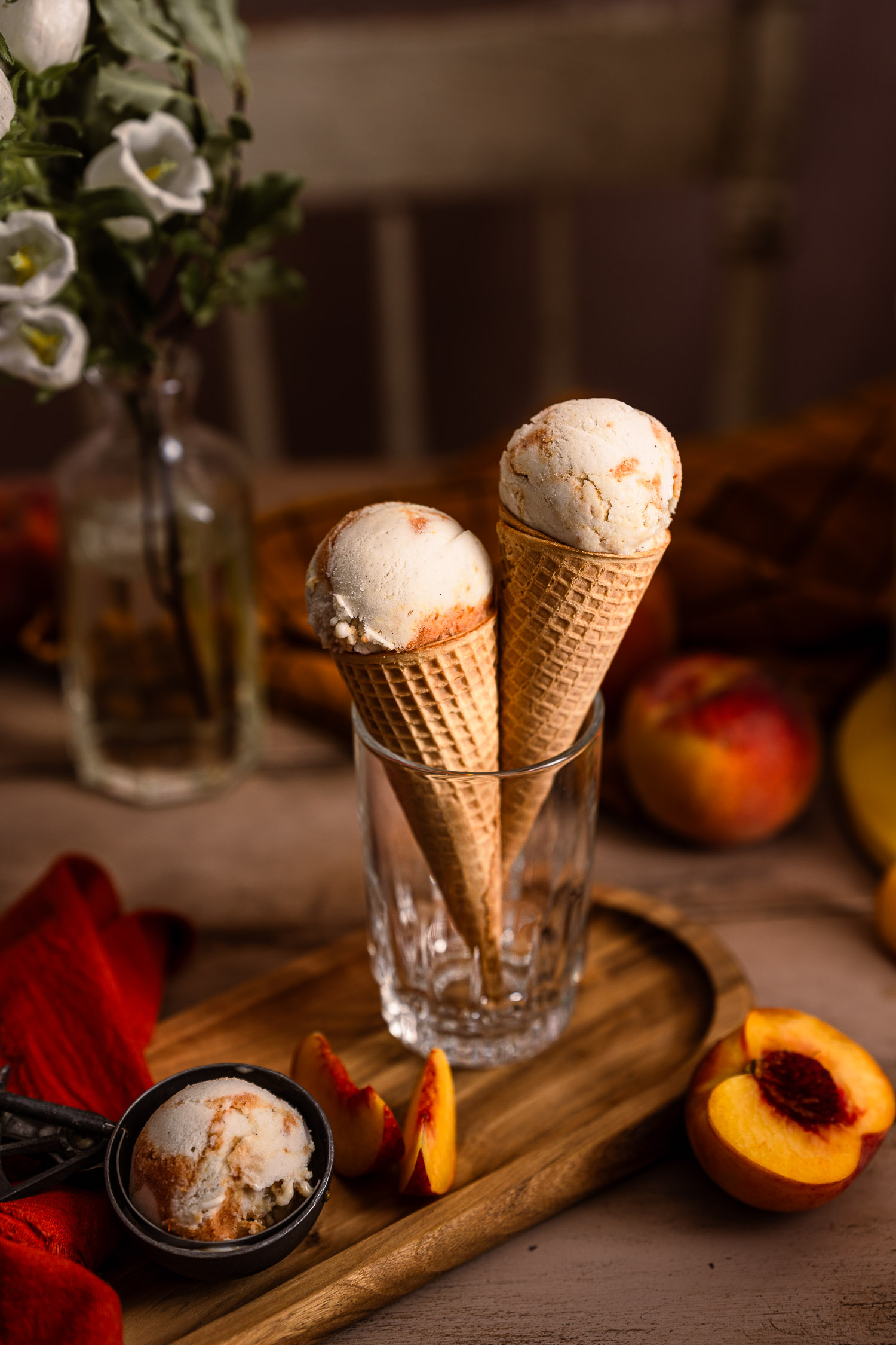 Two cones of Vegan Peaches and Cream Ice Cream on a table, surrounded by sliced peaches