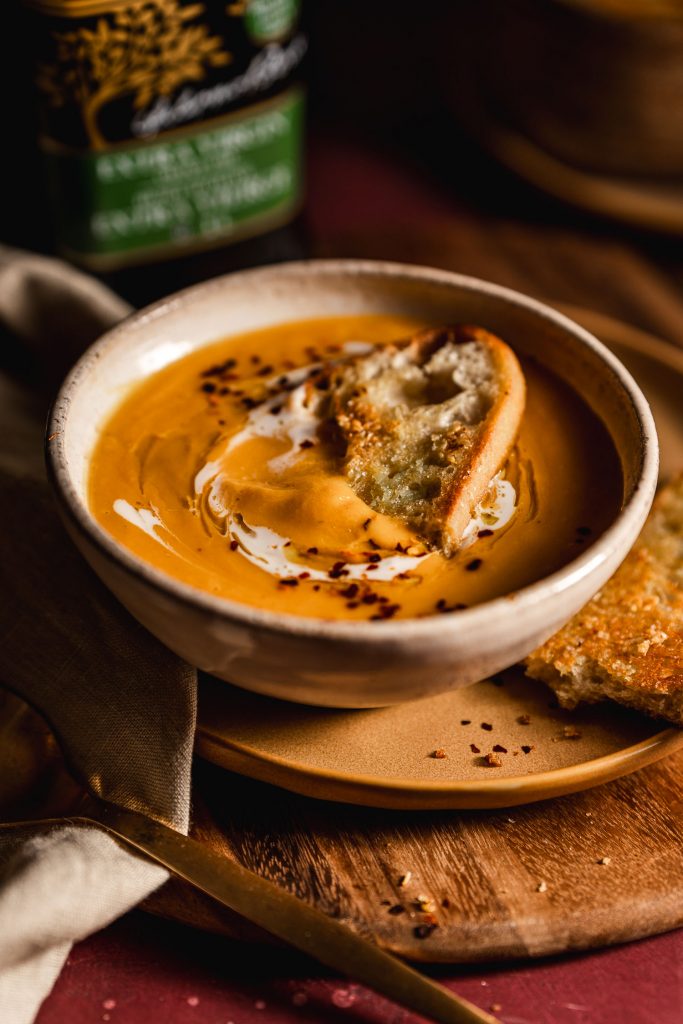 Close up of bowl of butternut squash with a slice of toasted bread floating in it.